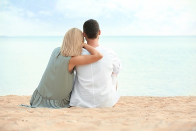 Happy romantic couple sitting together on beach, space for text