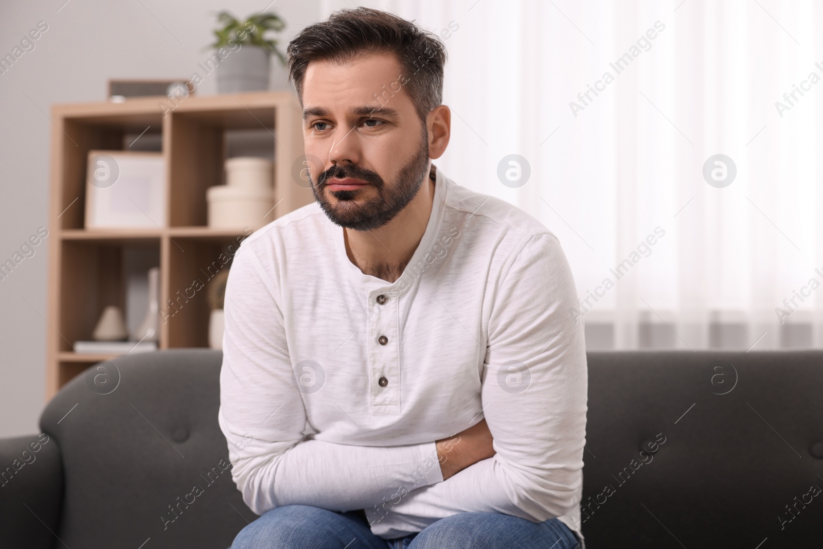 Photo of Unhappy man suffering from stomach pain on sofa at home