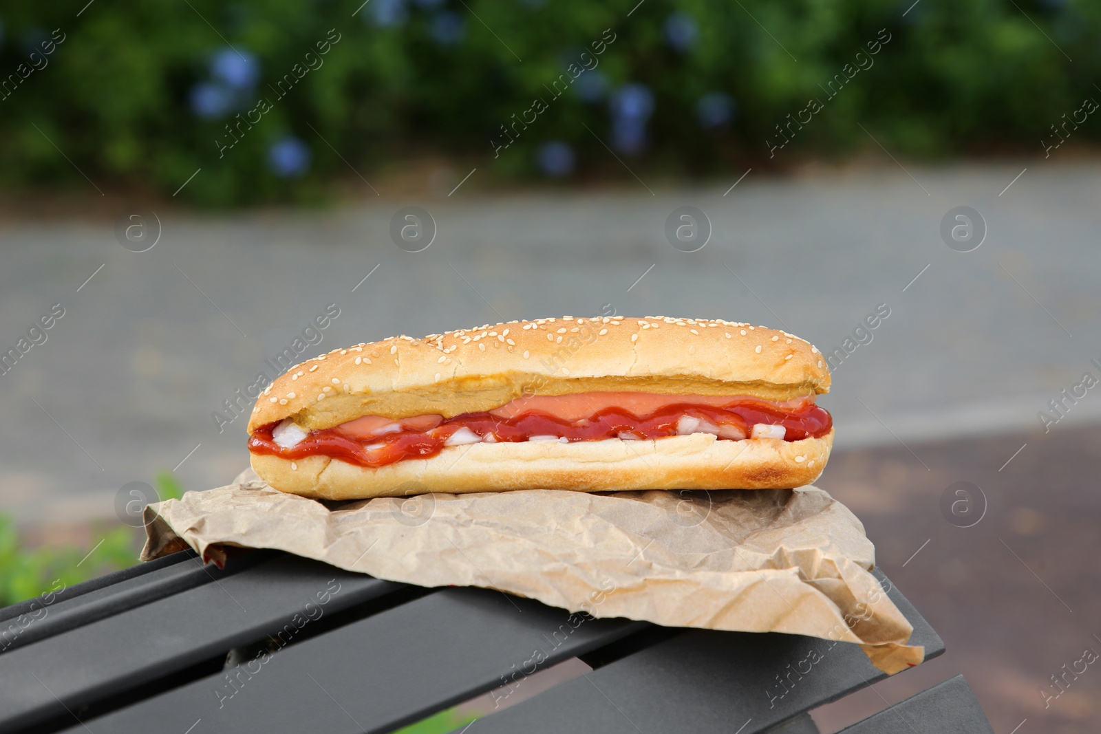 Photo of Fresh delicious hot dog with sauce on black bench outdoors