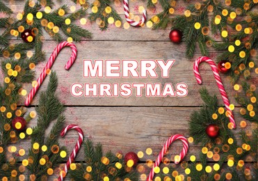 Greeting card with phrase Merry Christmas. Beautiful fir tree branches, candy canes and festive decor on wooden background, flat lay. Bokeh effect