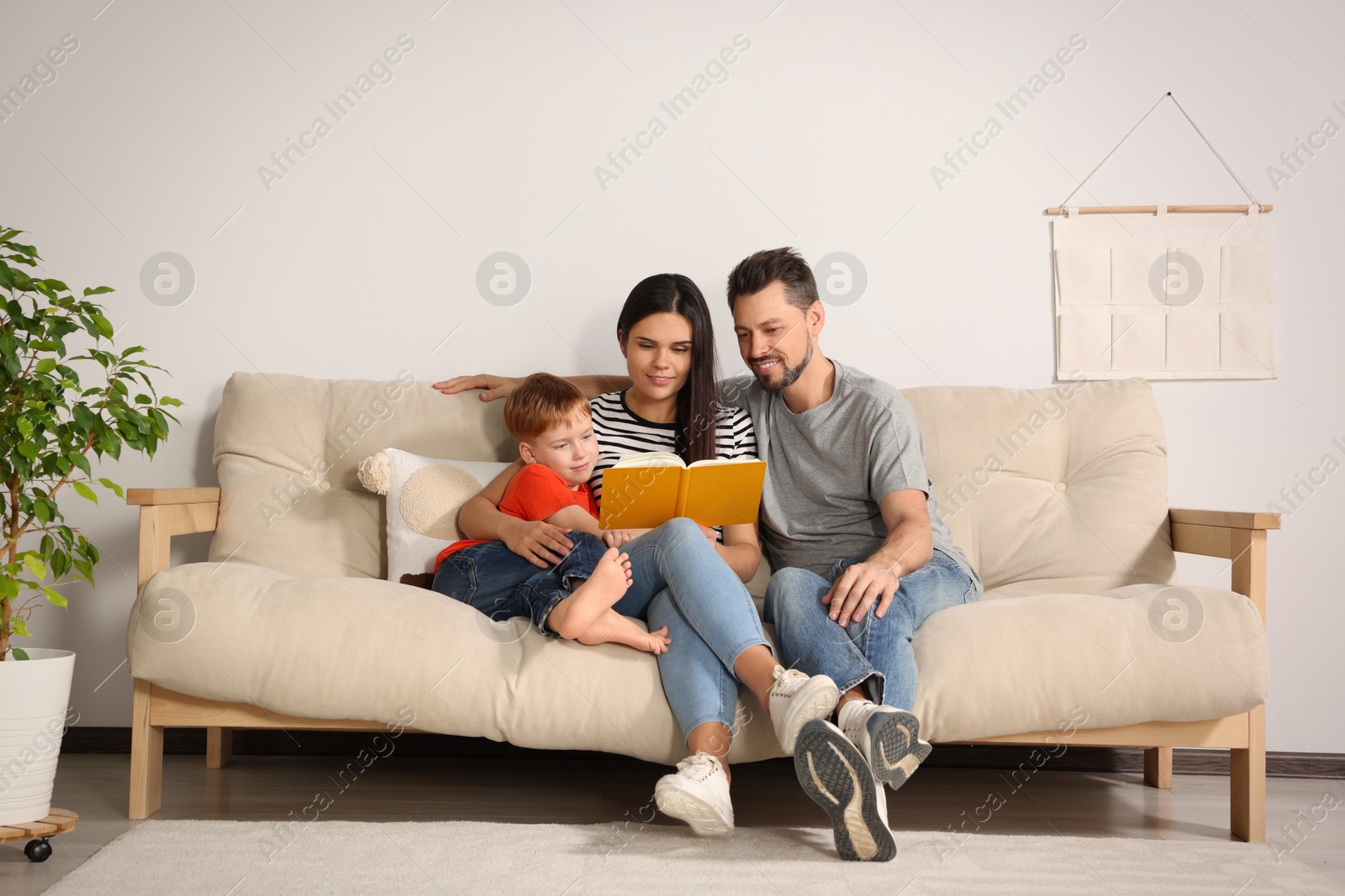 Photo of Happy family reading book together on sofa in living room at home