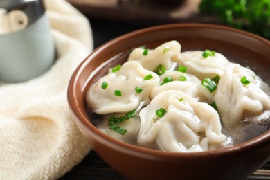 Photo of Bowl of tasty dumplings in broth on table, closeup. Space for text