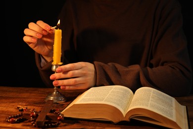 Photo of Woman lighting candle at table with Bible, closeup