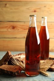 Photo of Bottles of delicious fresh kvass, spikelets and bread on blue wooden table
