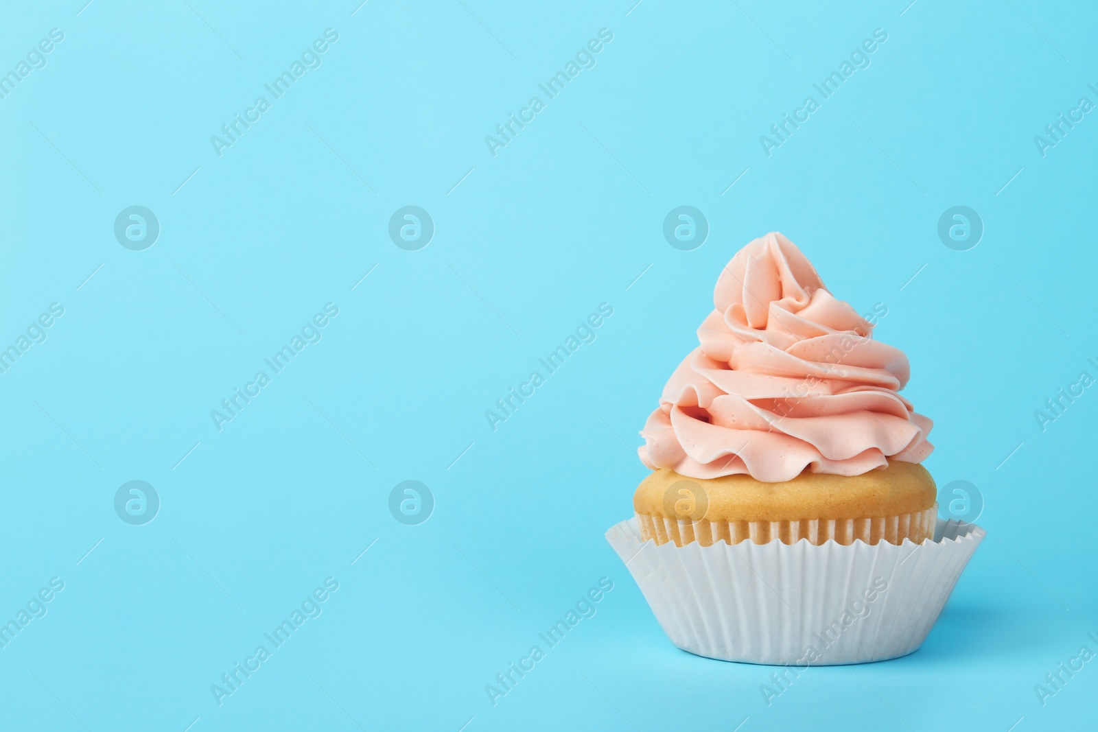 Photo of Tasty cupcake with cream on light blue background, space for text