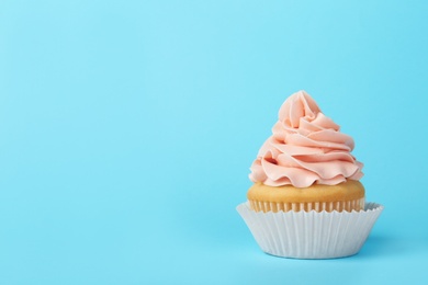 Tasty cupcake with cream on light blue background, space for text