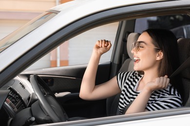 Photo of Listening to radio while driving. Beautiful young woman with stylish sunglasses enjoying music in car