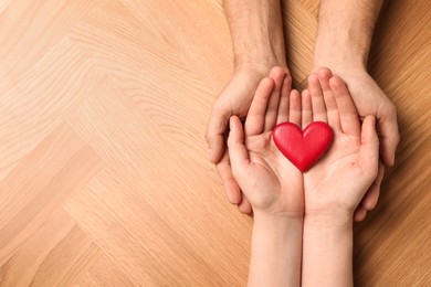 Couple holding red heart in hands at wooden table, top view. Space for text