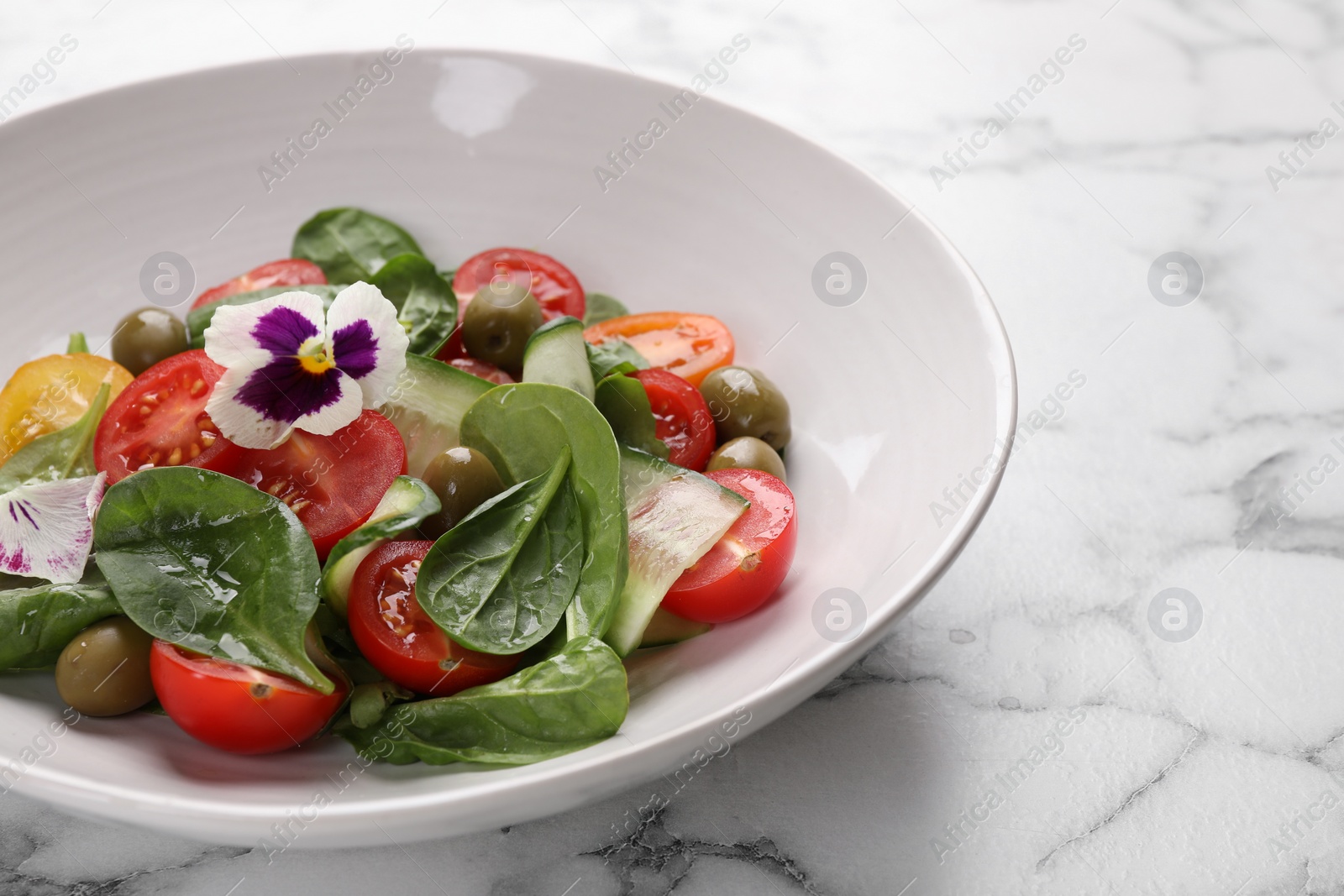 Photo of Delicious salad with vegetables and olives on white marble table, closeup