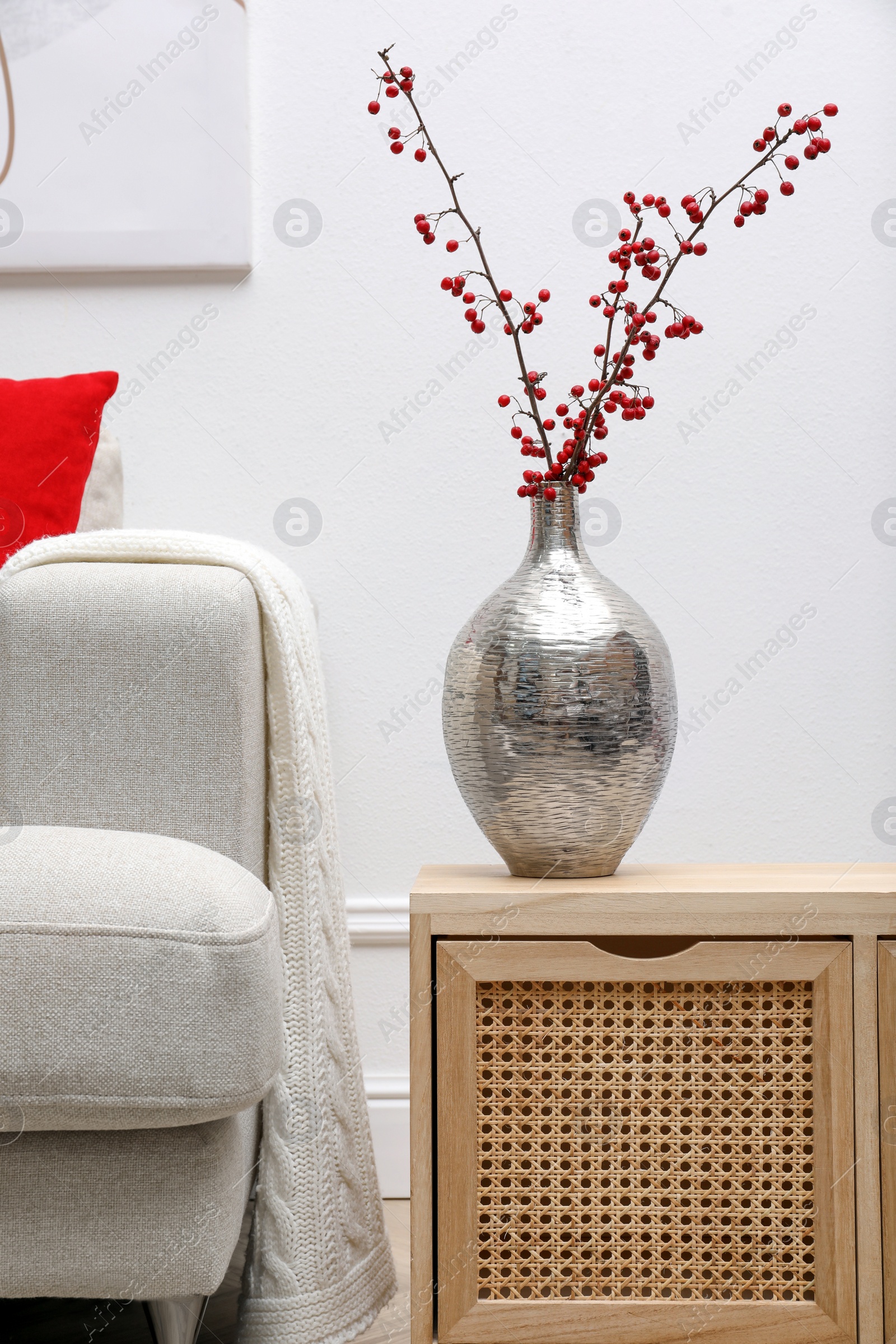 Photo of Hawthorn branches with red berries on wooden commode in living room