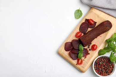 Photo of Delicious dry-cured beef basturma with basil, peppercorns and tomatoes on white table, flat lay. Space for text