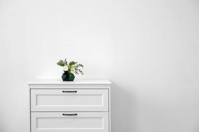 Photo of Modern chest of drawers with fresh flowers near wall. Space for text