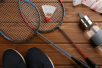 Photo of Rackets, sportswear and bottle on wooden table, flat lay. Playing badminton