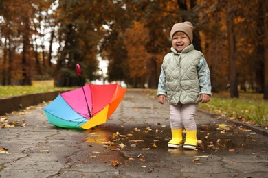 Photo of Cute little girl standing in puddle near colorful umbrella outdoors