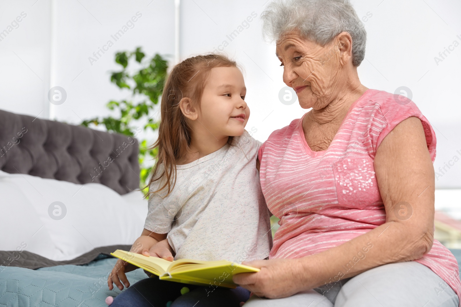 Photo of Cute girl and her grandmother reading book on bed at home