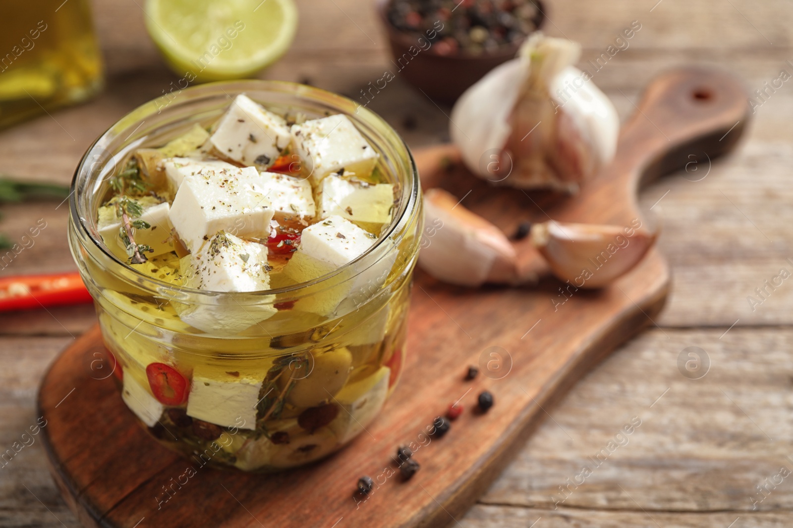 Photo of Glass jar of marinated feta cheese on wooden table