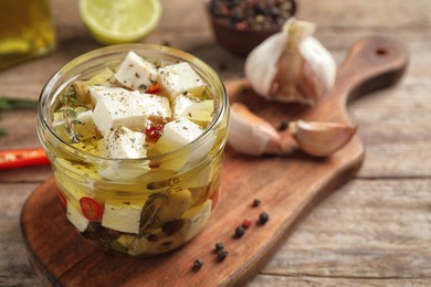 Glass jar of marinated feta cheese on wooden table