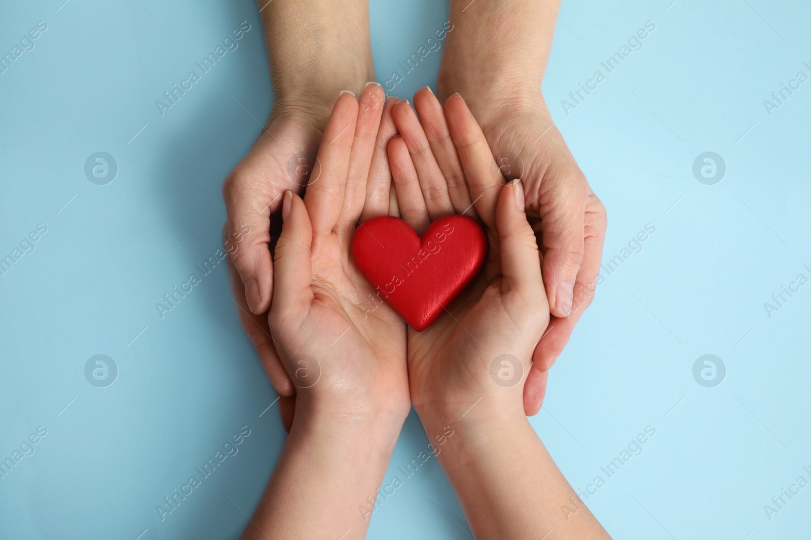 Photo of Young and elderly women holding red heart on light blue background, top view