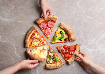 Women taking slices of different delicious pizzas at grey marble table, top view