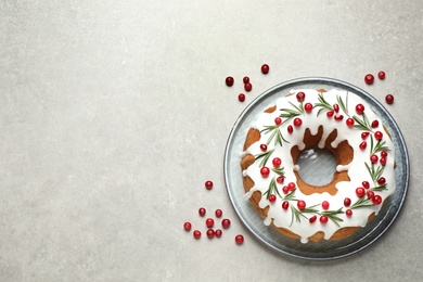 Traditional Christmas cake decorated with glaze, pomegranate seeds, cranberries and rosemary on light grey table, flat lay. Space for text