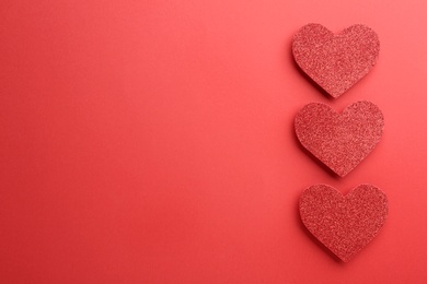 Shiny paper hearts on red background, flat lay. Space for text