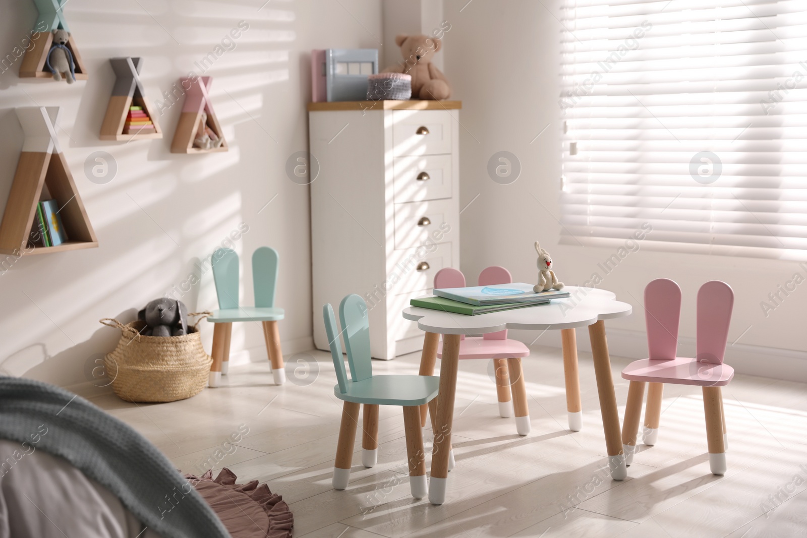 Photo of Small table and chairs with bunny ears in children's room interior