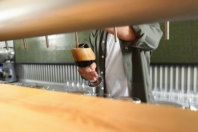 Bartender pouring fresh beer into glass in pub, closeup