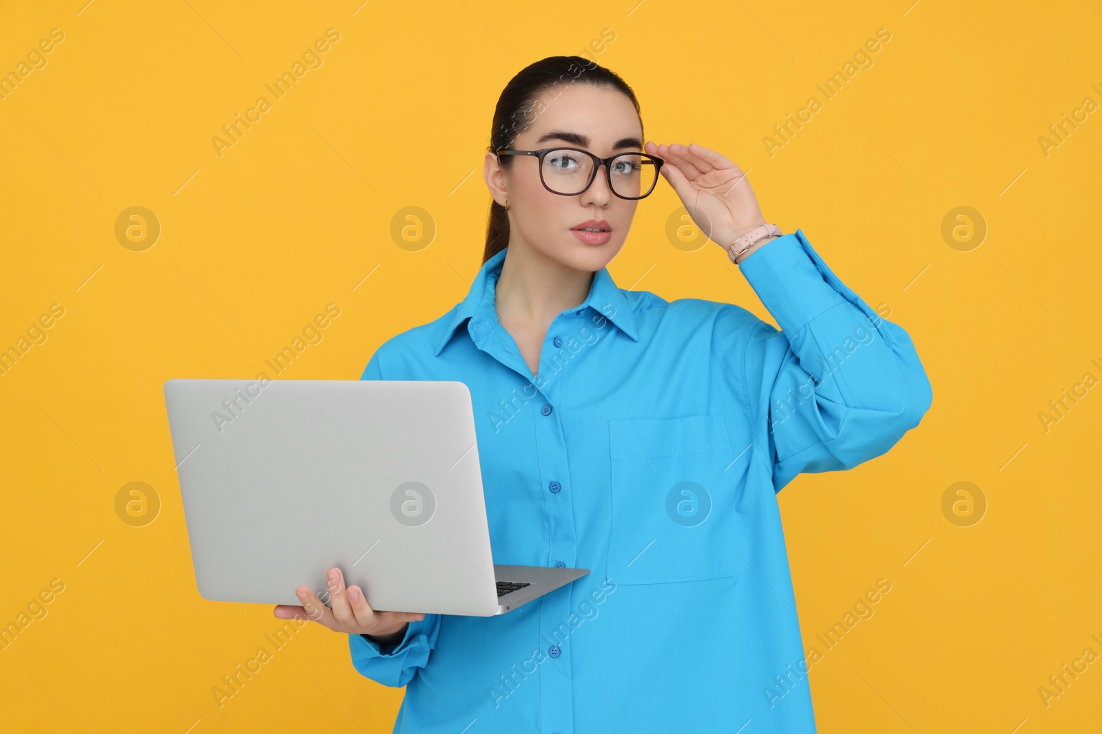 Photo of Young female intern with laptop on yellow background