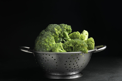 Photo of Tasty fresh broccoli in colander on table against black background