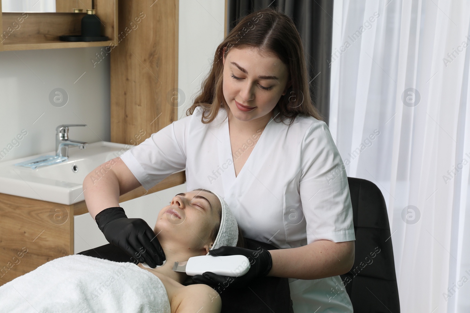 Photo of Cosmetologist using ultrasonic scrubber. Client having cleansing procedure in clinic