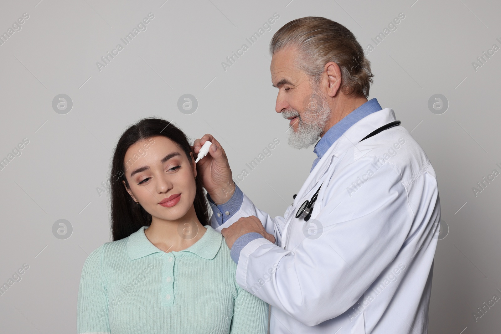 Photo of Doctor dripping medication into woman's ear on light grey background