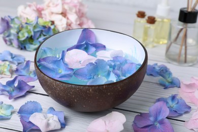 Spa composition. Aromatic water in bowl and flowers on white wooden table, closeup