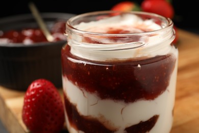 Tasty yoghurt with jam and strawberries on wooden board, closeup