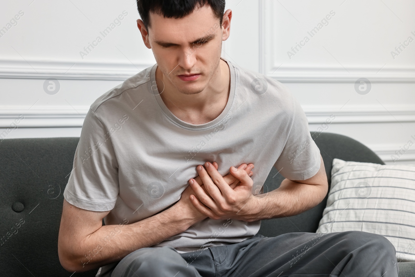 Photo of Young man suffering from heart hurt on sofa at home