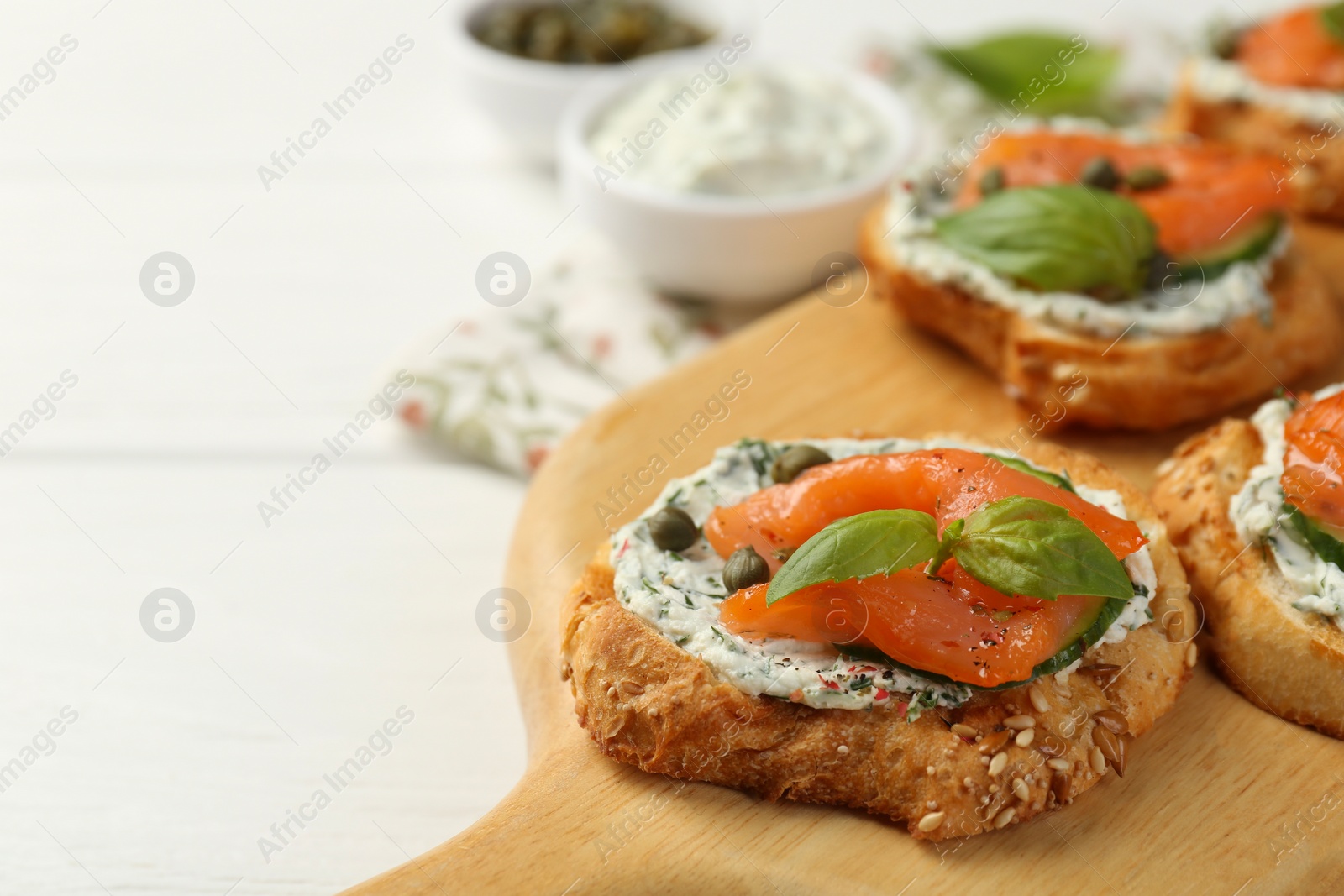 Photo of Tasty canapes with salmon, capers, cucumber and sauce on table, closeup. Space for text