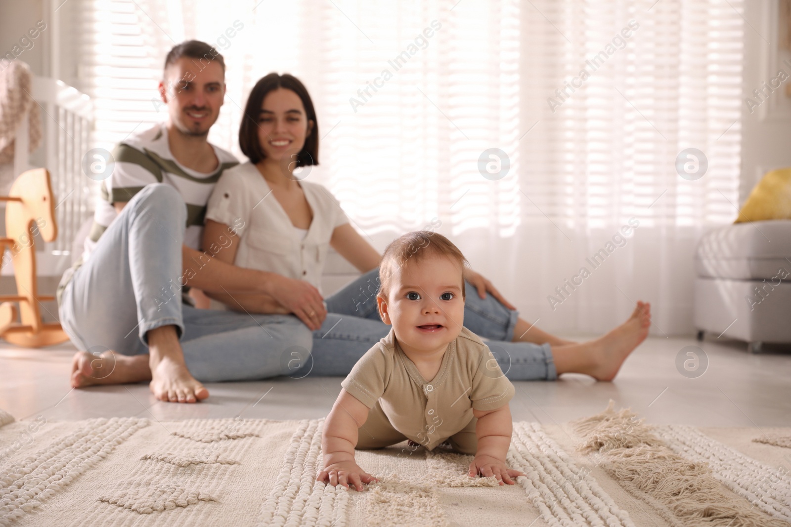 Photo of Happy parents watching their cute baby crawl on floor at home