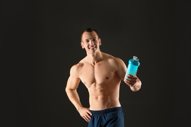 Athletic young man with protein shake on black background
