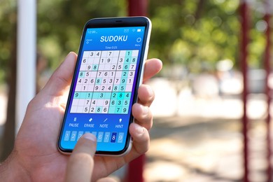 Image of Man playing sudoku game on smartphone outdoors, closeup