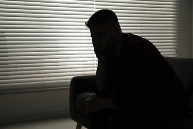 Photo of Silhouette of sad man near closed blinds indoors. Space for text