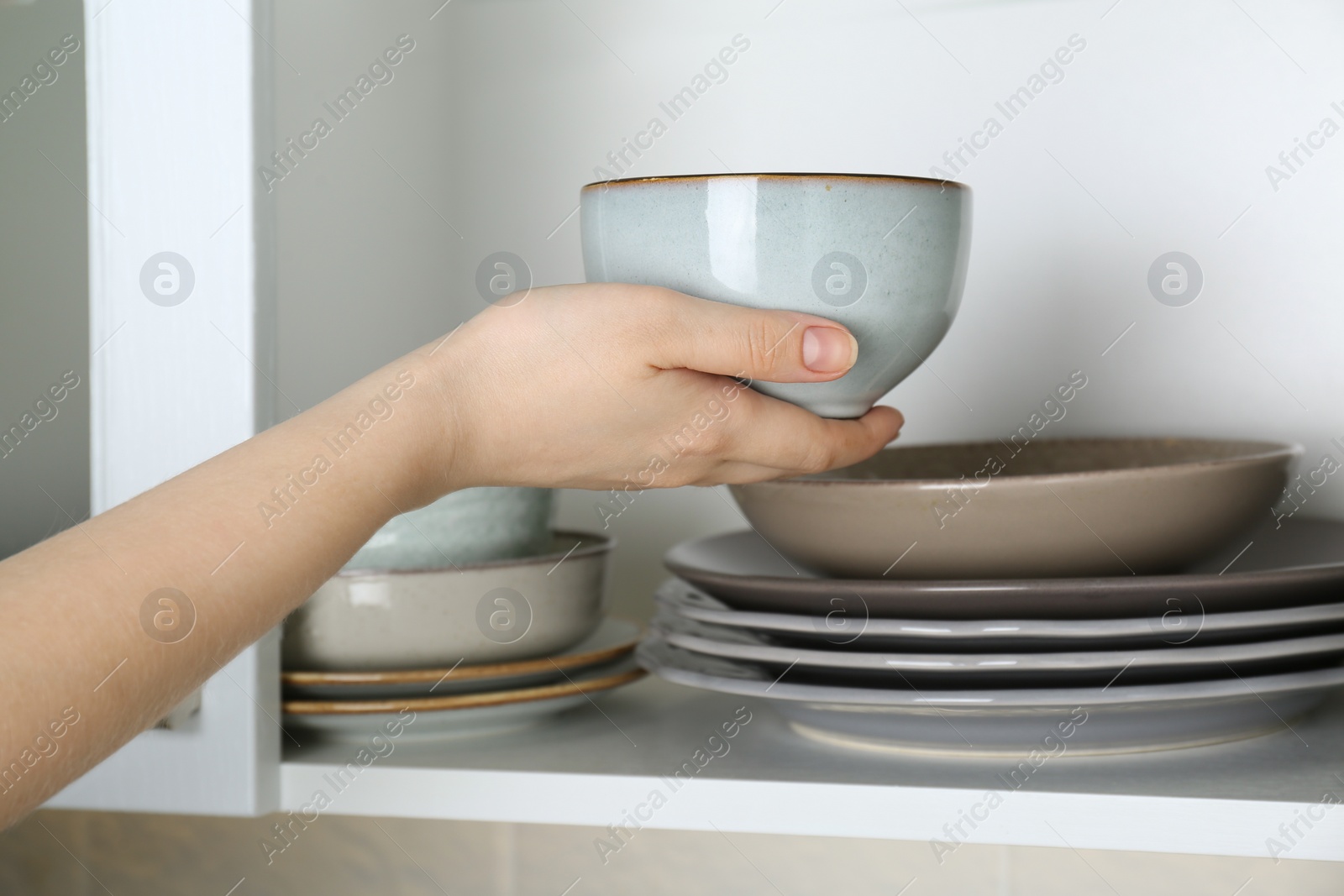 Photo of Woman taking ceramic bowl from cabinet at home, closeup