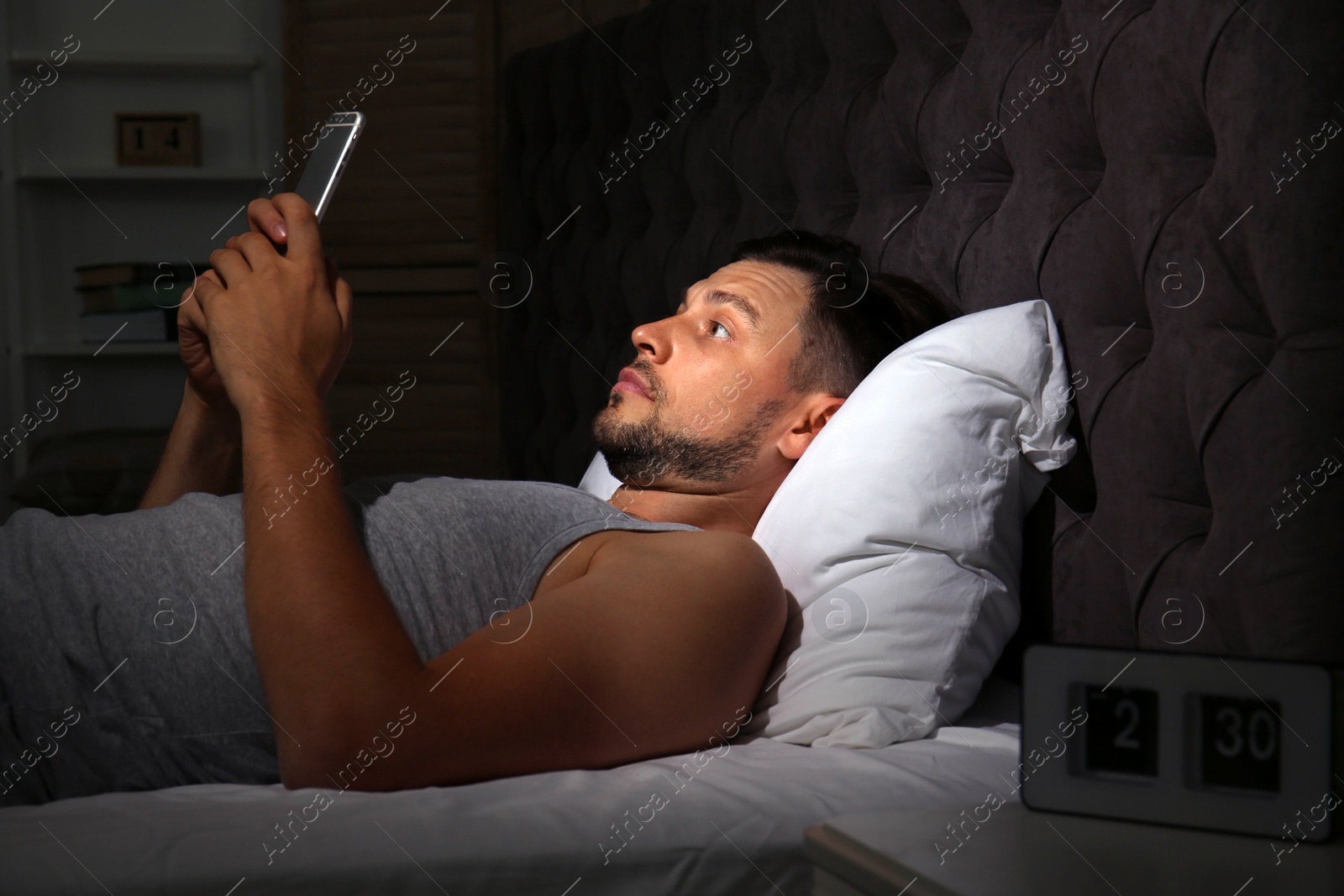 Photo of Man with smartphone lying in bed at home. Sleep disorder