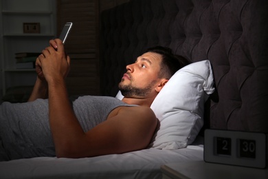 Photo of Man with smartphone lying in bed at home. Sleep disorder