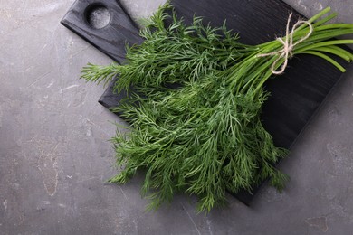 Photo of Board with bunch of fresh dill on grey textured table, top view. Space for text