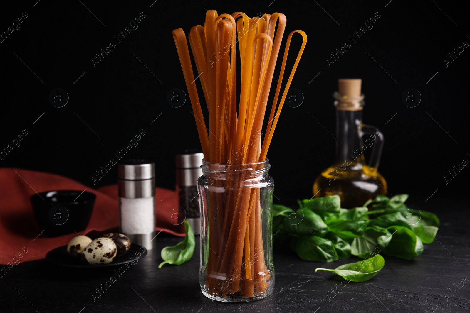 Photo of Uncooked buckwheat noodles and fresh ingredients on black table