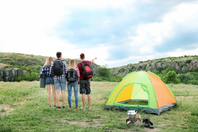 Group of young people with backpacks near camping tent in wilderness