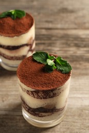 Photo of Tasty tiramisu and mint in glasses on wooden table, closeup