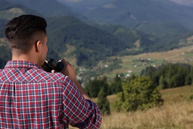 Photo of Man with binoculars in mountains on sunny day, back view