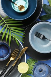 Photo of Flat lay composition with stylish ceramic plates and floral decor on blue background