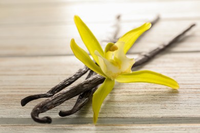 Vanilla pods and beautiful flower on white wooden table, closeup