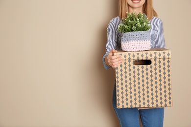 Woman with moving box and plant on color background. Space for text
